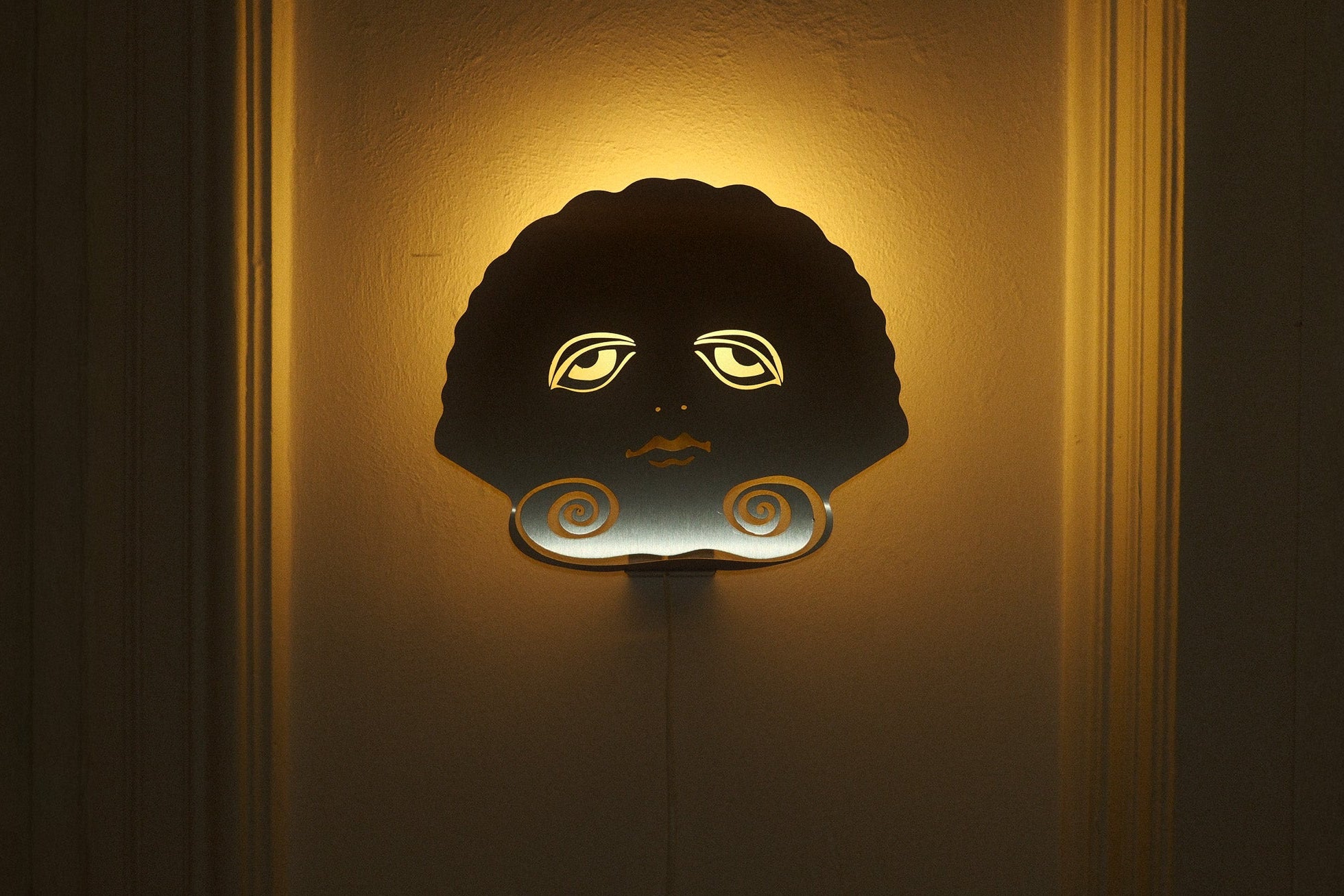 Decorative wall light with a face design on a textured wall.